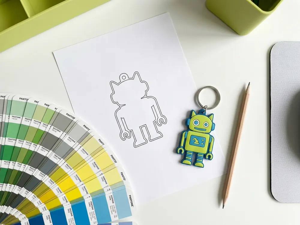 Scrivania con il disegno vettoriale per creare portachiavi personalizzati, la mazzetta Pantone e il portachiavi in PVC finito