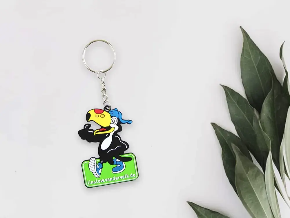 Portachiavi promozionale in PVC con mascotte gialla e nera e logo aziendale, accanto a una pianta