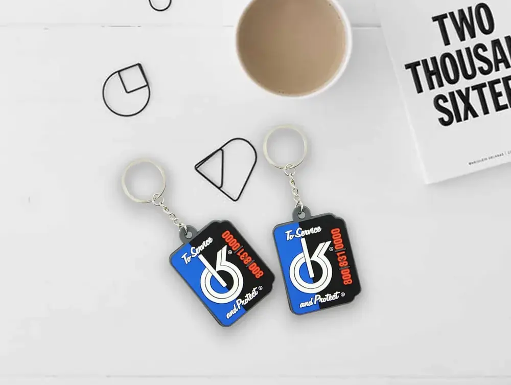 Due portachiavi in PVC personalizzati blu e rossi con logo sportivo, su un tavolo con una tazza di caffè