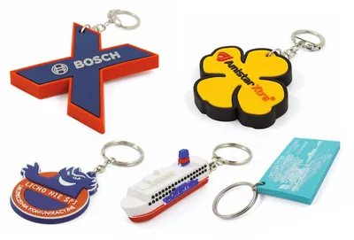 Cinque portachiavi PVC di forme diverse: una croce, un fiore giallo, uno stemma tondo, una nave bianca e una targhetta azzurra
