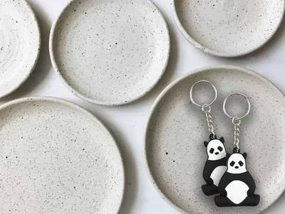 Due portachiavi PVC a forma di panda bianco e nero, appoggiati su un piattino di ceramica
