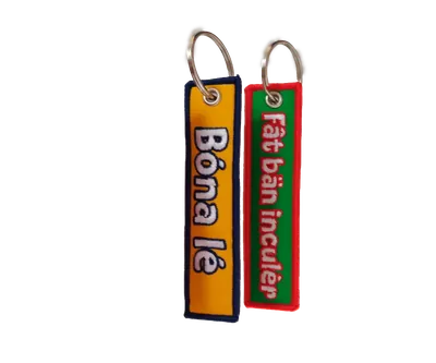 Due portachiavi in tessuto ricamato, uno giallo bordato di blu e uno rosso bordato di verde, scritti sui due lati